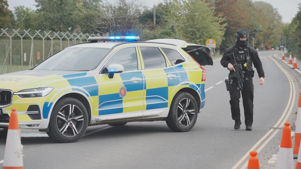 Armed police officer and marked police vehicles holding a road near RAF Fairford